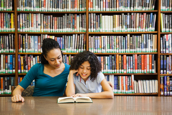 Mother helping daughter read book in library